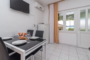 A dining area with a table set for two, a TV mounted on the wall, an air conditioner, and a view of the outdoors through a window. - Apartments Vin (Seget)