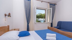 Une chambre avec un lit, un canapé bleu, une fenêtre donnant sur la mer et une lampe fixée au mur.