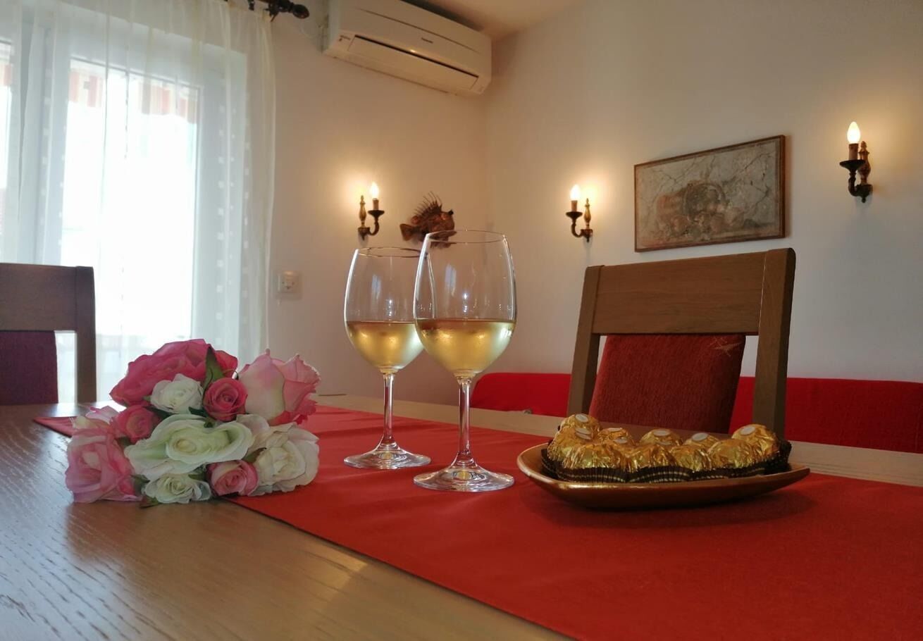 A dining table with a red tablecloth, two wine glasses, a bouquet of roses, and a plate of chocolates.