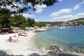A beach with clear water, a red and white boat, and a red building with people. - Apartment Milena (Okrug)