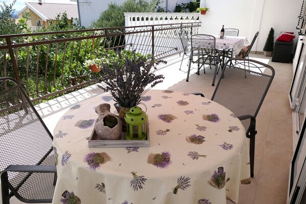 A round table with a floral tablecloth, surrounded by metal chairs, on a balcony with a metal railing. - Apartment Milena (Okrug)