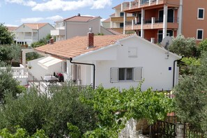 A white house with a tiled roof, surrounded by greenery and adjacent multi-story buildings. - Apartment Milena (Okrug)