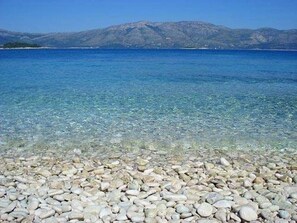 Una spiaggia ciottolosa con acqua cristallina e montagne in lontananza.