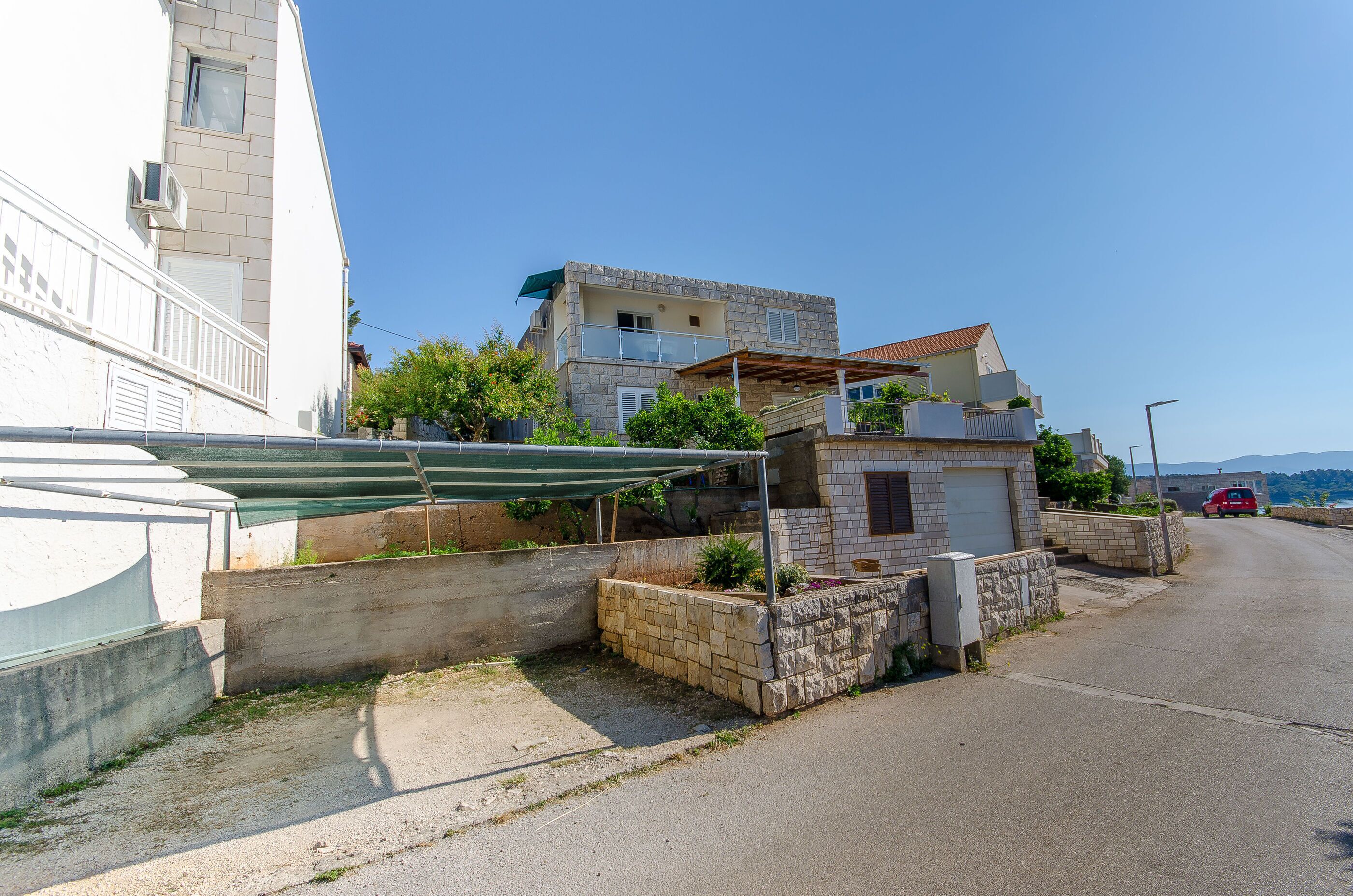 Une rue résidentielle avec une maison à deux étages, un petit jardin et une voiture rouge garée.