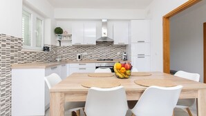 Een moderne keuken met witte kastjes, een betegelde spatwand en een houten eettafel met witte stoelen.