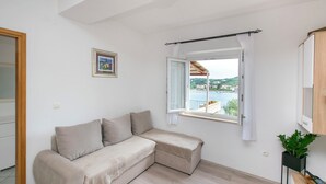 Een moderne kamer met een beige modulaire bank, een raam met uitzicht op water en gebouwen, en een kleine plant op een bijzettafeltje.