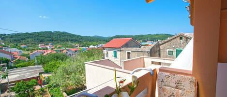 A balcony with a view of a village, a wicker basket with flowers, and a wooden table.