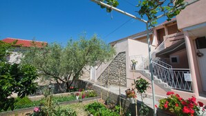 A residential building with a stone staircase, a balcony, and a garden with various plants and flowers. - Apartment Neno (Preko)
