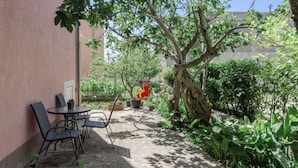 Un patio con mesa y sillas, rodeado de follaje y un árbol.