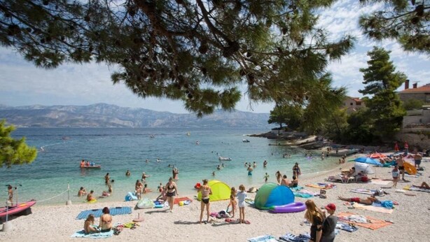 Ein Strand mit Menschen, die sich sonnen, schwimmen und spielen. Sonnenschirme, Strandtücher und ein Zelt sind vorhanden.