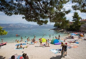 A beach with people sunbathing, swimming, and playing. There are umbrellas, beach towels, and a tent. - Apartments Damir (Postira)