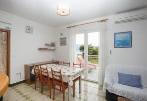 A dining area with a table and chairs, a sofa, a balcony with a view, and a clock on the wall. - Apartments Damir (Postira)