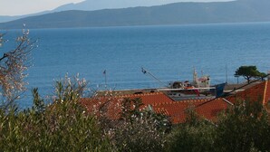 A coastal view with a boat docked near a building with a red-tiled roof. - Apartment Bianca (Podgora)