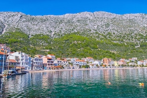 A coastal town with buildings along the waterfront, a clear blue sky, and a mountain in the background. - Apartment Bianca (Podgora)