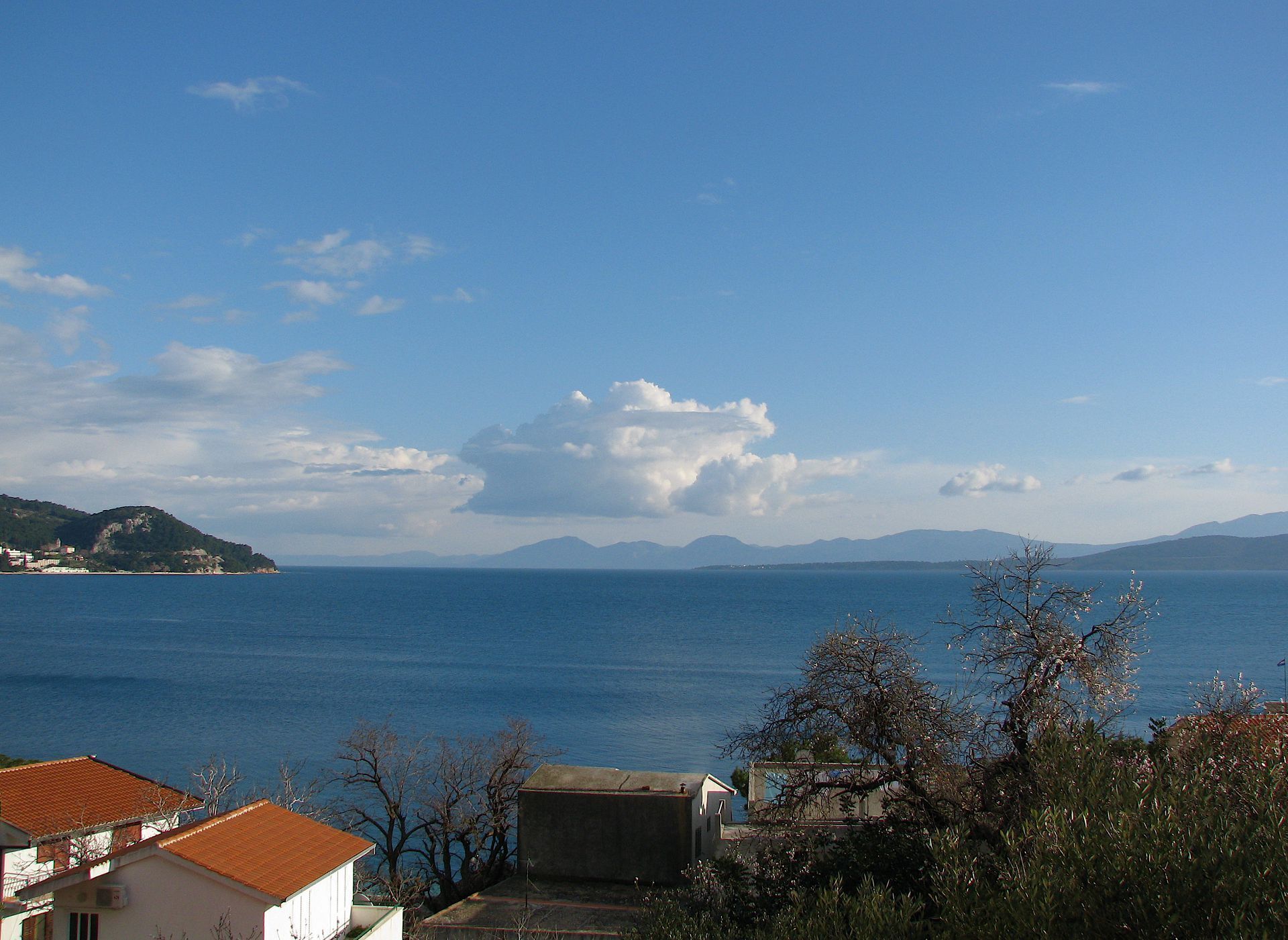 Vista costera con cielo despejado, mar tranquilo y montañas a lo lejos.