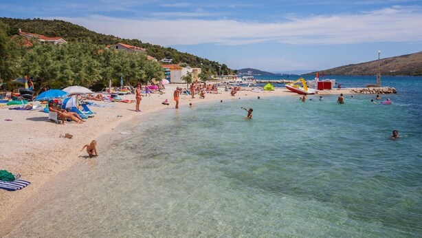 Una spiaggia con acque cristalline, persone che prendono il sole e barche.