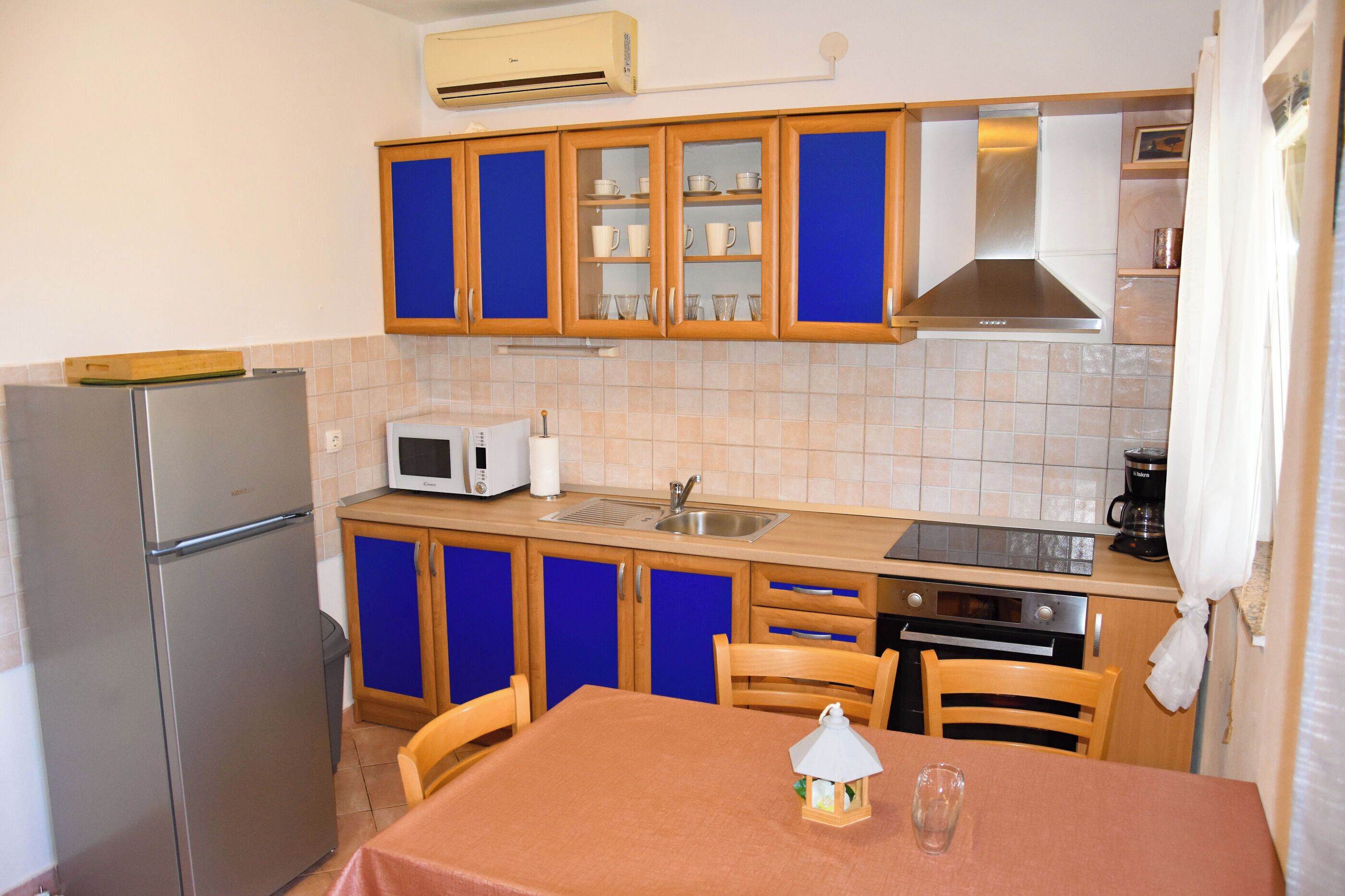 Eine kompakte Küche mit blauen Schränken, einem Kühlschrank, einer Mikrowelle, einem Spülbecken und einem Tisch mit Stühlen.