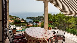 A balcony with a table and chairs, overlooking a scenic view of a lake and surrounding houses. - Apartment Ivope (Supetar)