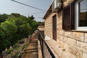 A stone building with a balcony, a staircase, and a garden with various plants. - Apartment Ivope (Supetar)