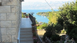 A stone staircase leading to a balcony with potted plants, overlooking a coastal landscape with a body of water and hills in the distance. - Apartment Ivope (Supetar)