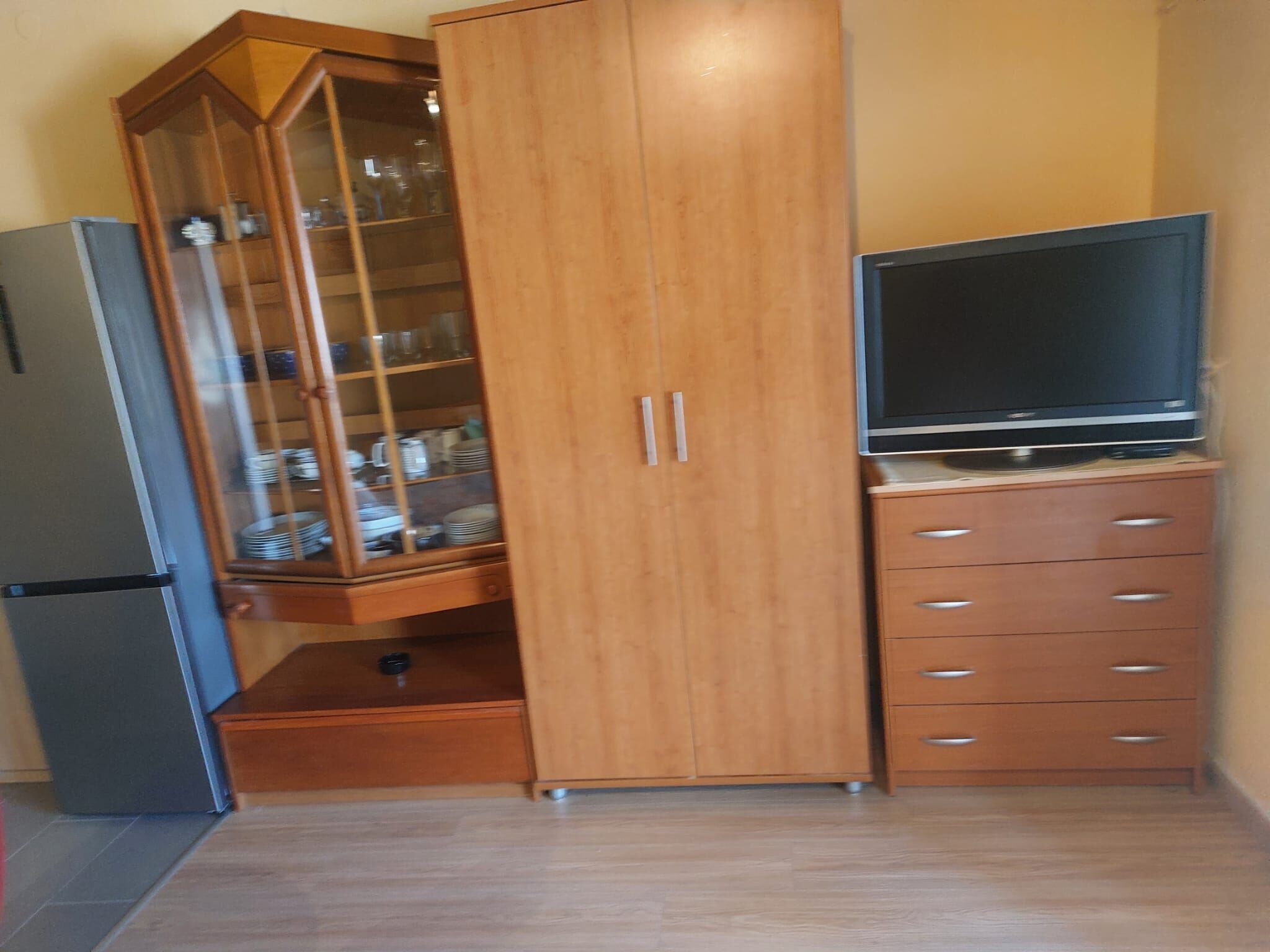 A kitchen with a wooden cabinet, a built-in refrigerator, and a television on a wooden stand.