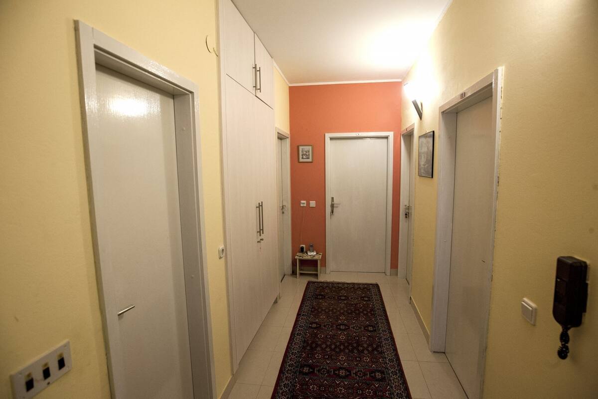 A narrow hallway with white doors on both sides, a patterned rug on the floor, and a small table with items on it.