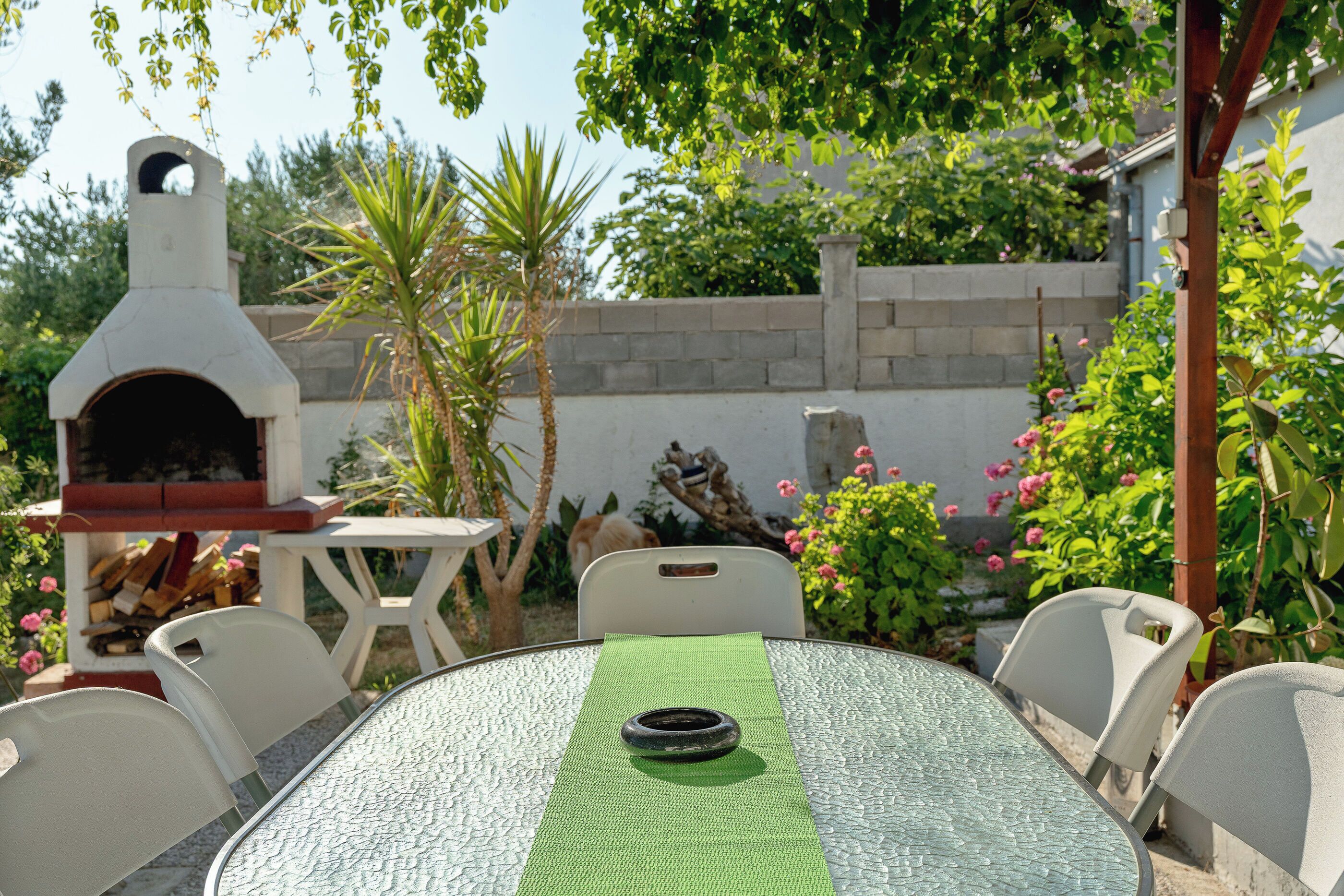 An outdoor patio with a round table, chairs, a pizza oven, and a brick wall.