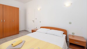 A bedroom with a bed, wooden wardrobe, bedside tables, and wall-mounted lights. - Apartments Marietta (Razanac)