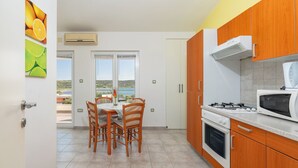 A kitchen with wooden cabinets, a gas stove, a microwave, and a dining area with a table and chairs. - Apartments Marietta (Razanac)