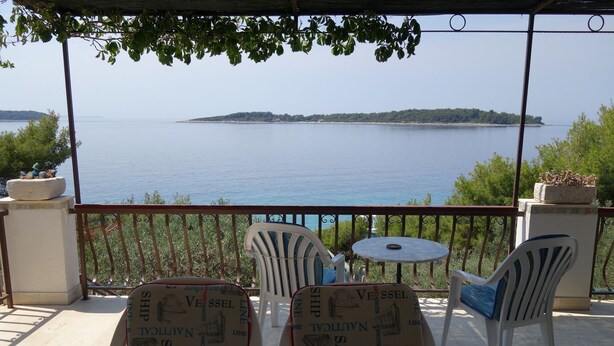 Una terraza con dos sillas y una mesa pequeña, con vistas al mar tranquilo y una isla distante.