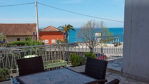 A balcony with wicker furniture, a view of the sea, and a building with a red roof. - Apartments and Rooms Robi (Podstrana)
