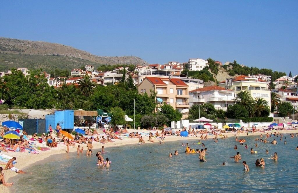 A coastal town with a beach, buildings, and a hilly backdrop.