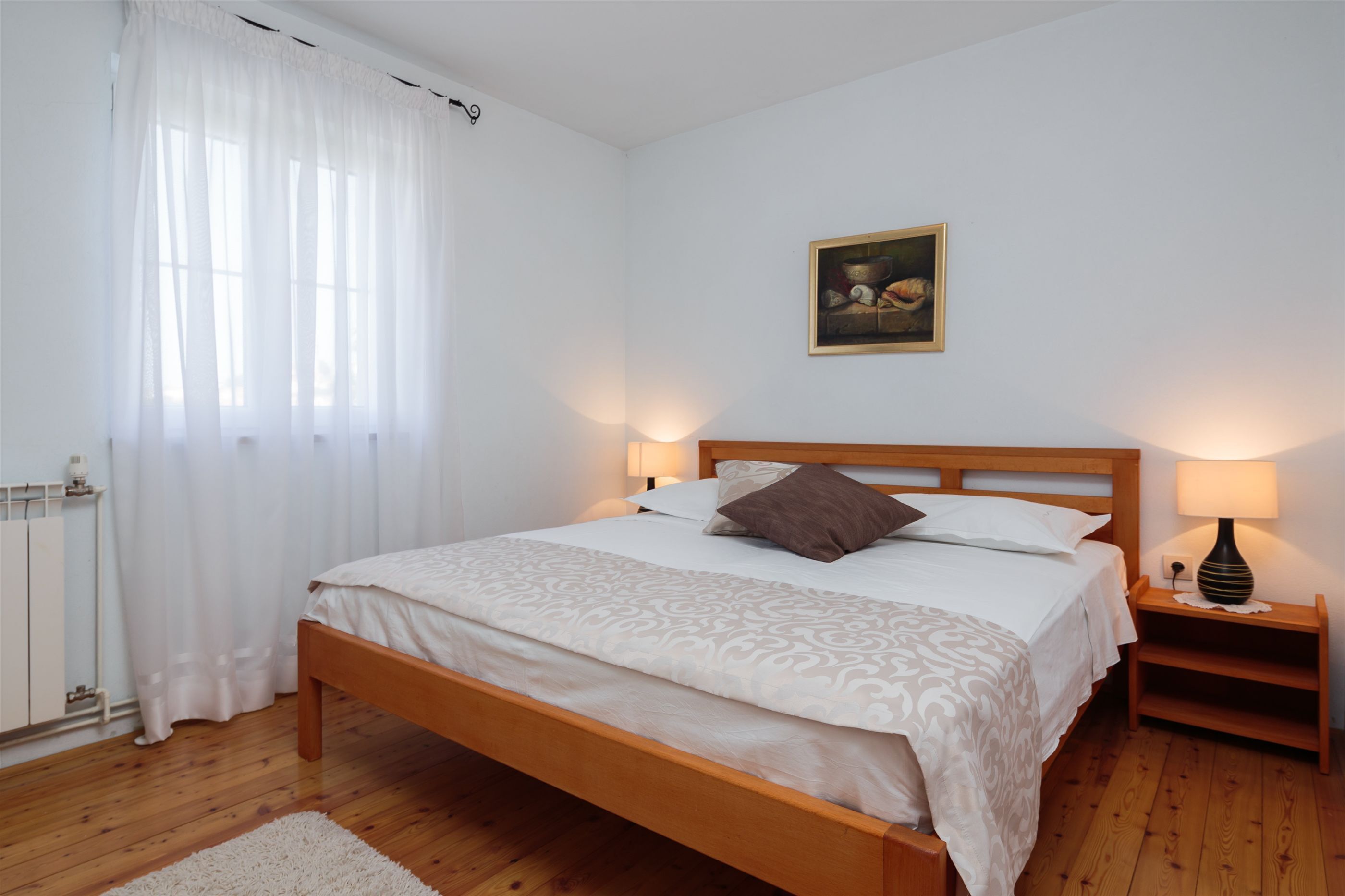 Un letto rifatto con cura, una testiera in legno, un comodino con una lampada e un quadro appeso al muro.