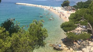 Ein Strand mit klarem Wasser, badenden Personen und einem sandigen Ufer.