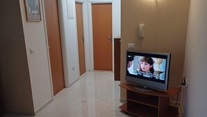Ein Flur mit einem Fernseher auf einem Holzboden, einer Wandleuchte und einer Tür am Ende.