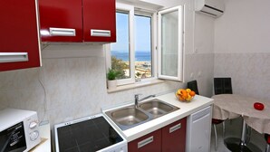 A compact kitchen with a view of the sea, a microwave, a sink, and a small dining area. - Apartment Marija (Trogir)