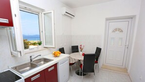 A compact kitchen with a view of the sea, a dining area with chairs, and a white door. - Apartment Marija (Trogir)