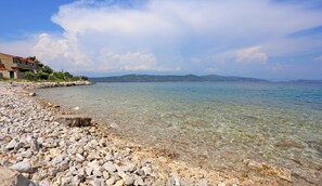 A rocky beach with clear water and a distant view of hills. - Apartment Marija (Trogir)