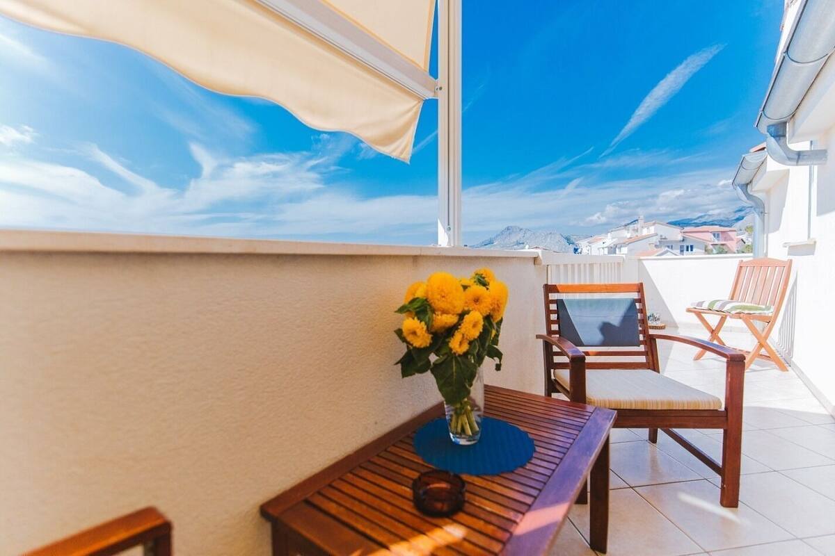 A balcony with a wooden table, two chairs, and a vase of yellow flowers.