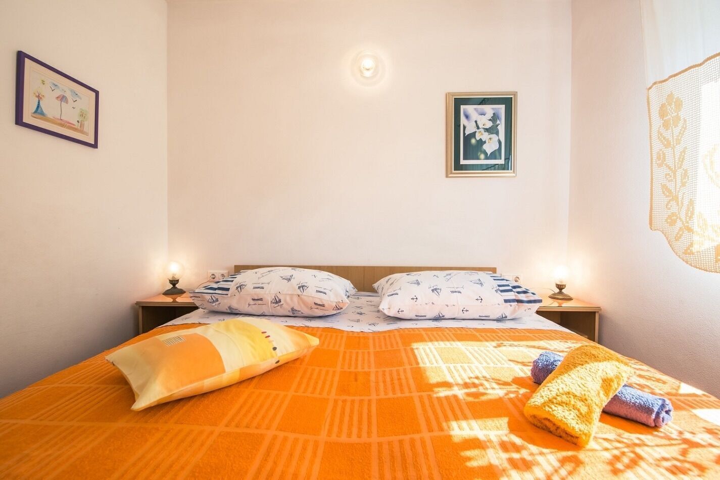 Una cama bien hecha con almohadones estampados, un tapiz decorativo y una lámpara de noche.