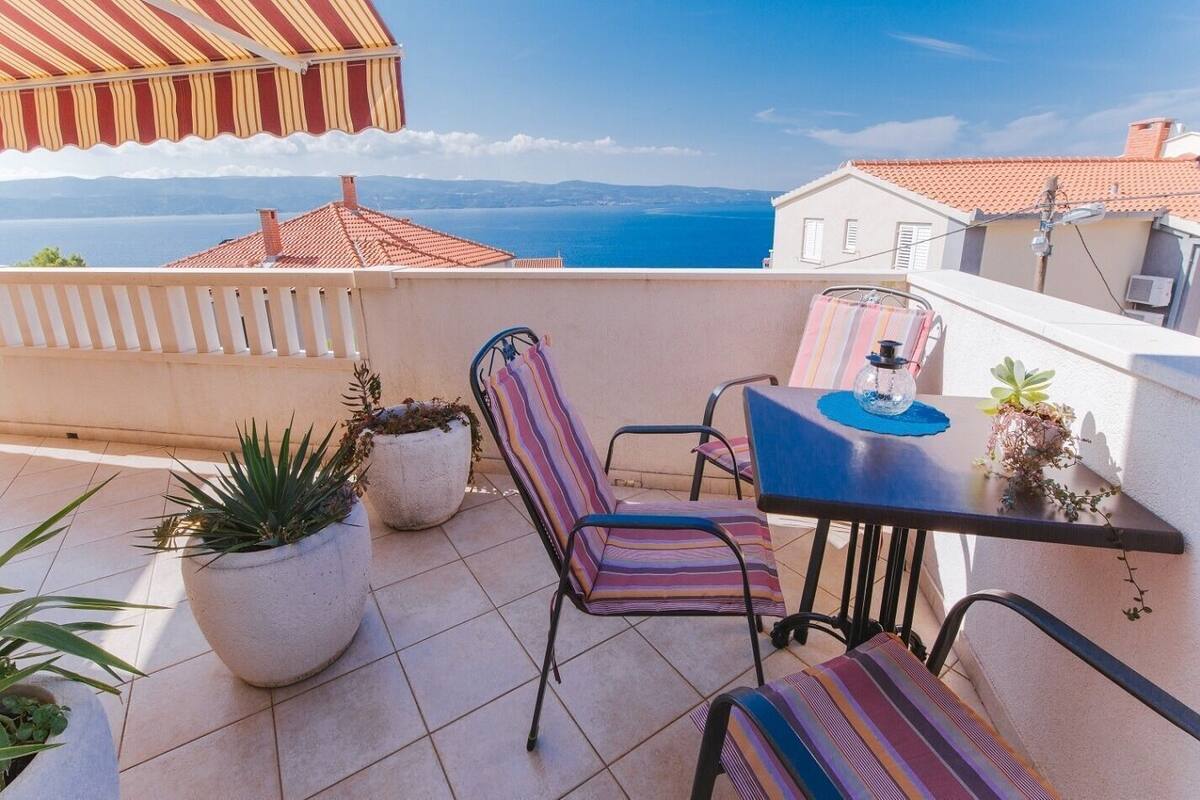 A terrace with a table and chairs, potted plants, and a view of the sea.