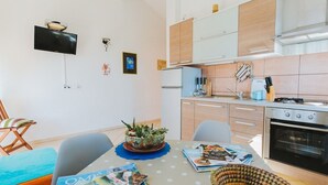Moderni keittiö, jossa on sisäänrakennettu uuni, ruokailutila kahdelle katetulla pöydällä sekä seinälle asennettu televisio.