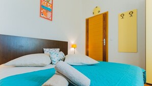 Hotellihuone, jossa on sänky, tyynyjä, seinäkello ja ovi.