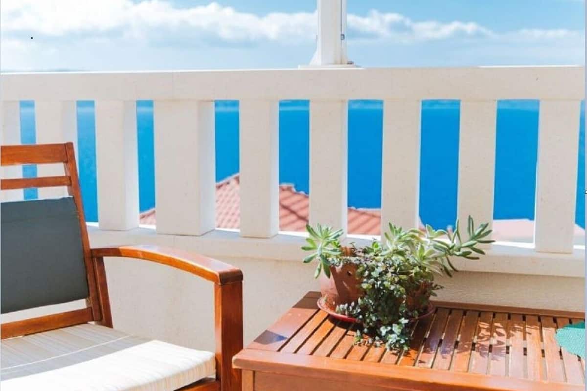 A wooden chair and table on a balcony with a view of the sky and a blue railing.