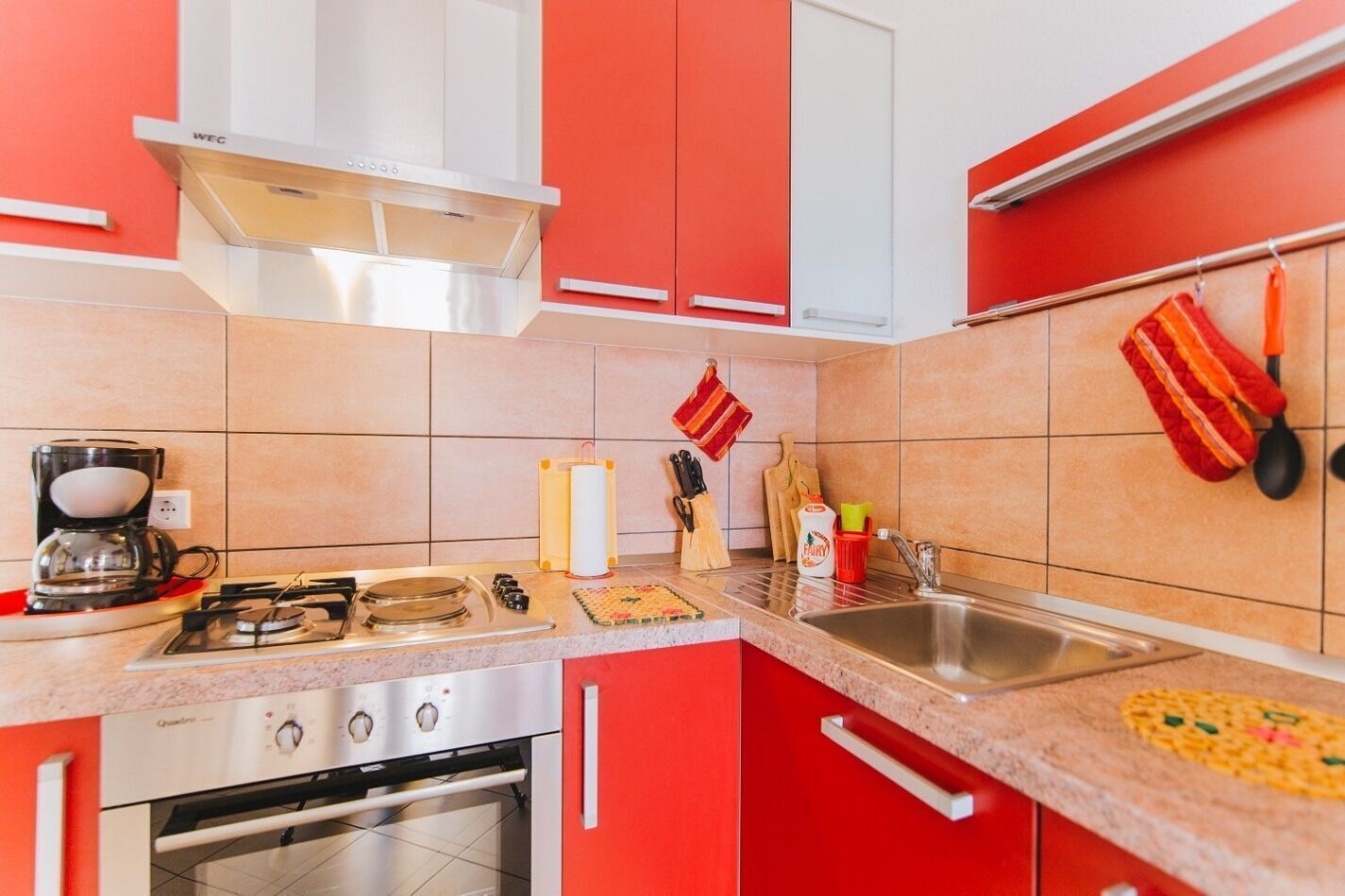 A kitchen with red cabinets, a gas stove, a coffee maker, and various kitchen utensils.
