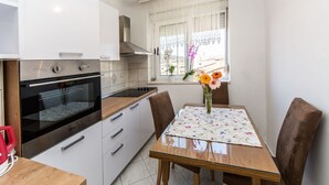 Une cuisine moderne avec des meubles blancs, un four noir et un plan de travail en bois. On y trouve une table à manger avec des chaises et un vase rempli de fleurs.