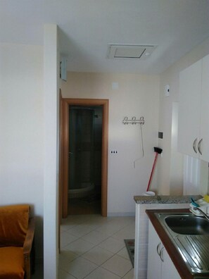 Una cocina compacta con un lavamanos, una escoba y una puerta que da al baño.