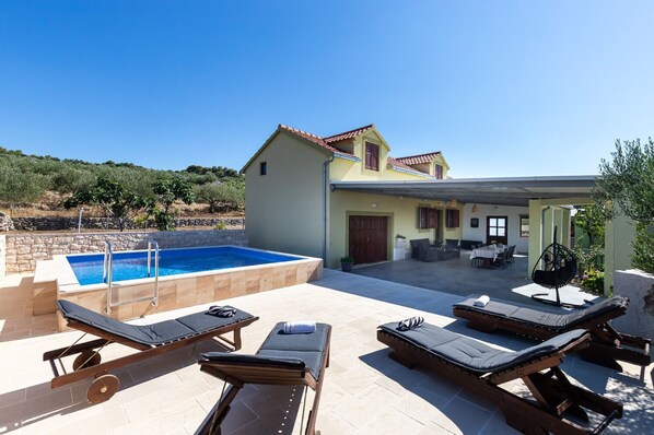 A poolside area with lounge chairs, a swimming pool, and a covered patio with outdoor seating. - House Mario (Supetar)