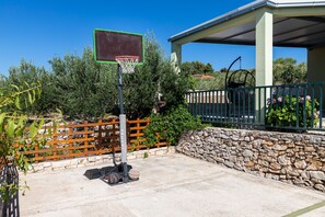 A basketball court with a hoop, surrounded by a stone wall and a wooden fence. - House Mario (Supetar)