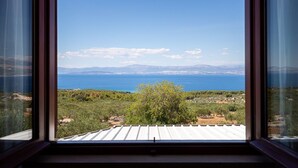 Uitzicht door een raam op een kustlandschap met heldere lucht, verre bergen en een wateroppervlak.
